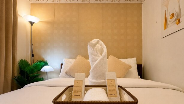 Ein Hotelzimmer mit einem ordentlich bezogenen Bett, einem Willkommenskorb und einer Lampe.