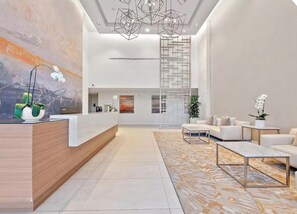 A modern reception area with a wooden reception desk, a large abstract painting, and a seating area with sofas and a coffee table. - Breathtaking, rare 3-bedroom condo at Luxury Amrit Ocean Resort on Singer Island (Singer Islad)