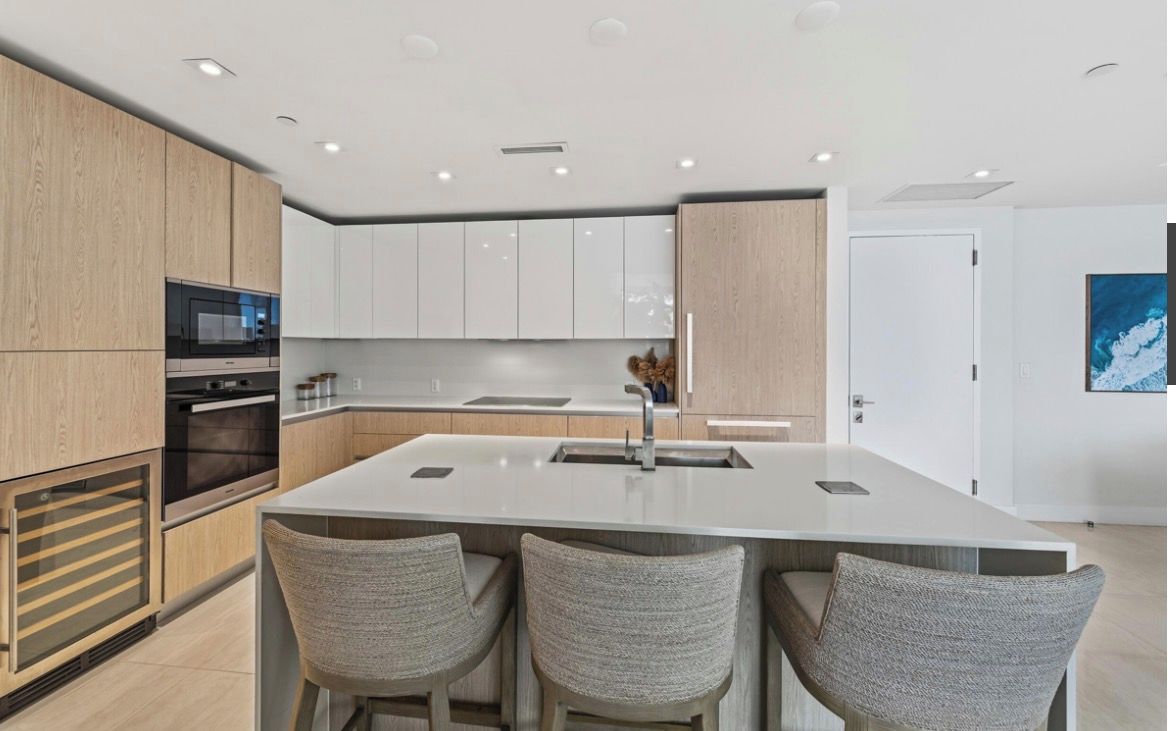 A modern kitchen with a central island, built-in appliances, and a seating area with three chairs.