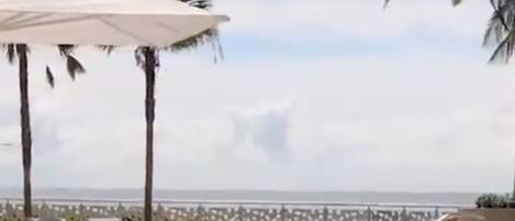 A pool area with lounge chairs and umbrellas, a view of the ocean, and a fence.