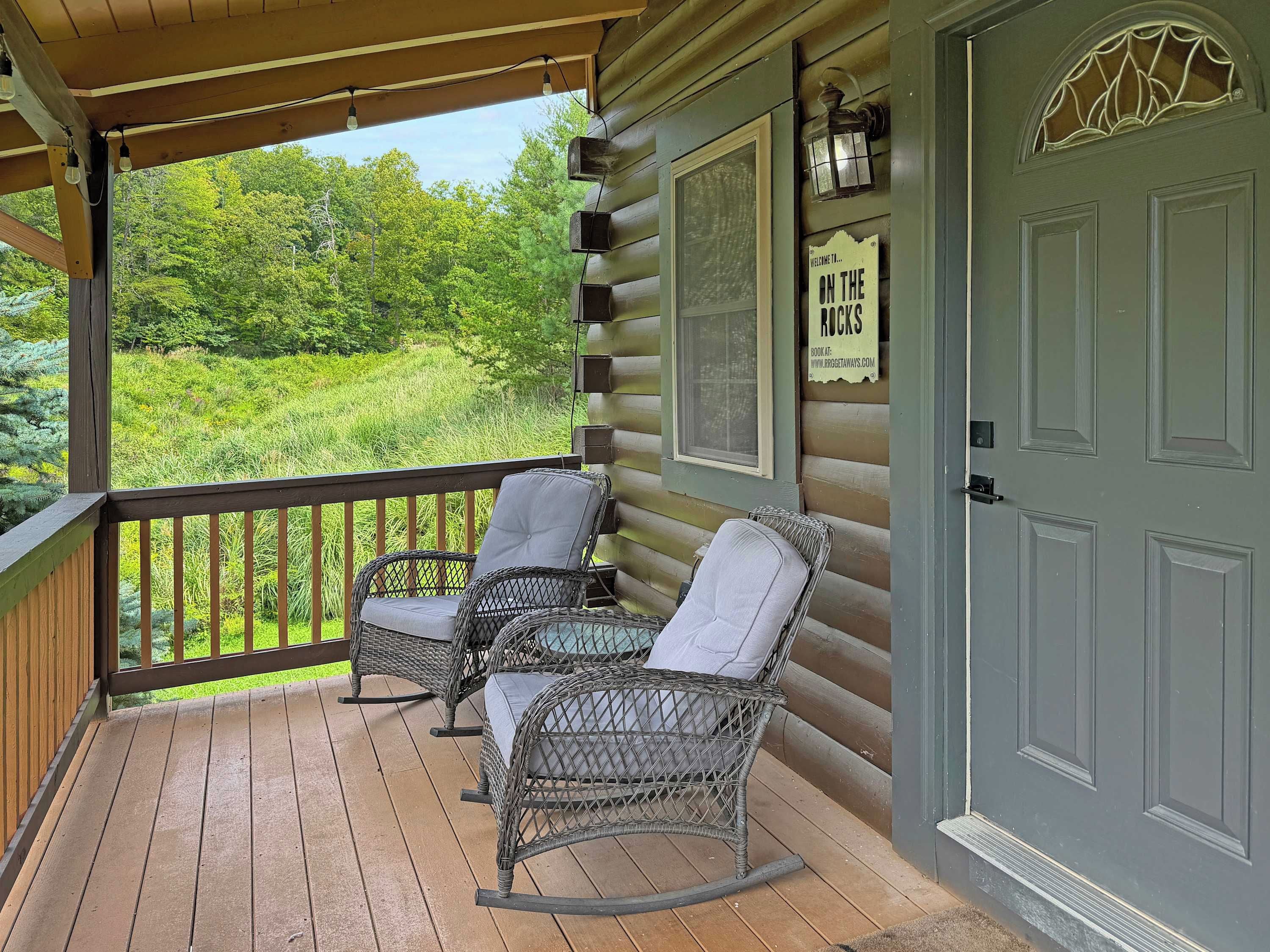 A wooden porch with wicker rocking chairs and a sign that reads 'Welcome to... ON THE ROCKS'.