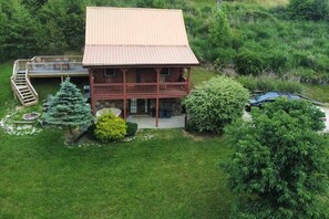 Eine zweistöckige Blockhütte mit einem Balkon, umgeben von einem gepflegten Rasen und verschiedenen Bäumen.