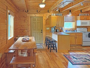 Ein Interieur einer Holzhütte mit Essbereich, Küche und einer Tür mit der Aufschrift 'ON THE ROCKS'.