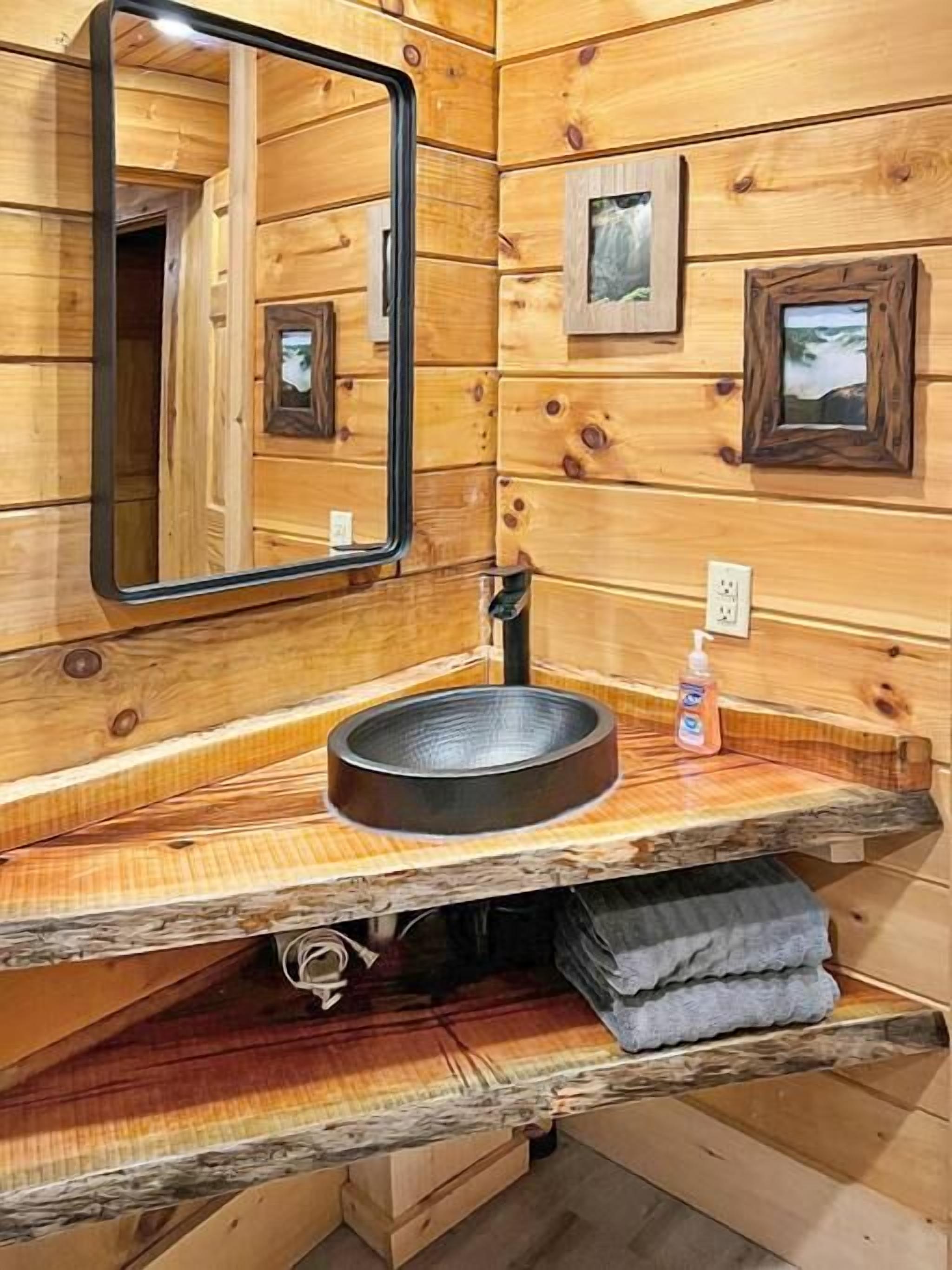 Ein Holzhütten-Interieur mit einem spiegelnden Holzrahmen, einem Waschbecken aus Metall und einem Handtuchhalter.