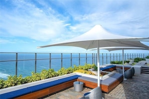 A rooftop terrace with a view of the ocean, outdoor seating, and a large umbrella. - Cozy Studio for 3 | 50m to Surfers Beach (Surfers Paradise)