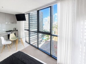A modern kitchen with a flat-screen TV, a dining area with a glass table and chairs, and a large window with a city view. - Cozy Studio for 3 | 50m to Surfers Beach (Surfers Paradise)