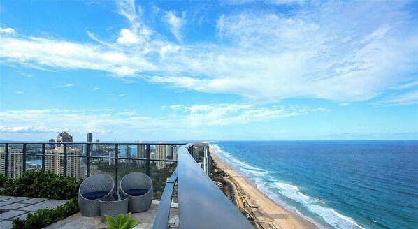 Un balcon avec des fauteuils en osier donnant sur une plage et l’océan.