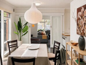 A dining area with a table set for two, a hanging light fixture, and a view into the living room. - 3BR Belmont House | Walk to High St Shops (Belmont)