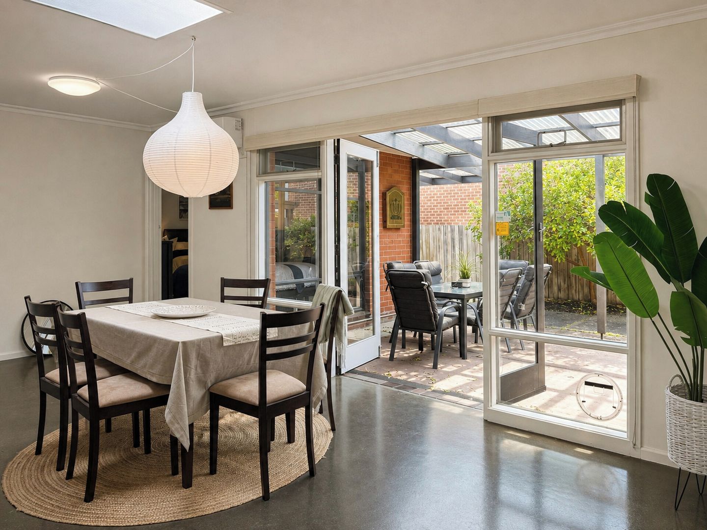 A dining area with a table set for six, a hanging light fixture, and a view through a glass door to an outdoor patio.
