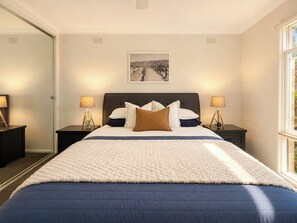 A hotel room with a large bed, two bedside tables with lamps, a framed picture on the wall, and a window with a view. - 3BR Belmont House | Walk to High St Shops (Belmont)