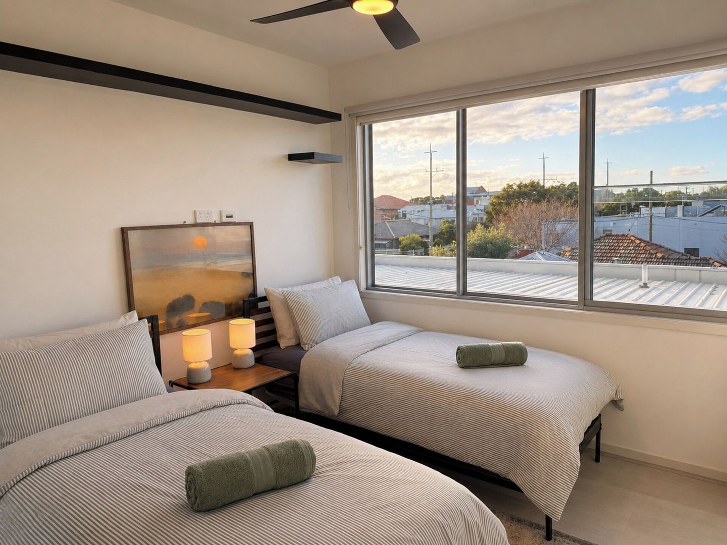 Une chambre d’hôtel avec deux lits, un ventilateur de plafond, un tableau et une vue sur le paysage urbain.
