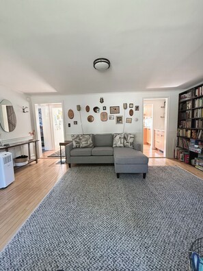 A living room with a grey sectional sofa, a large rug, and a bookshelf filled with books. - Sun-Filled Brick Townhouse Near Downtown Bath (Bath)
