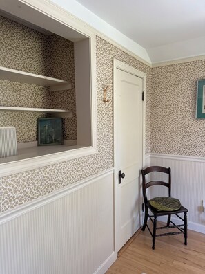 A room with a door, a chair, a shelf with a framed picture, and patterned wallpaper. - Sun-Filled Brick Townhouse Near Downtown Bath (Bath)