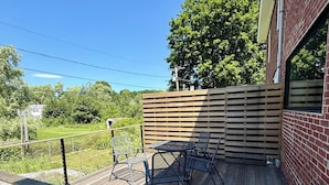 Une terrasse en bois avec une table et des chaises, une rambarde en métal et un mur en briques.