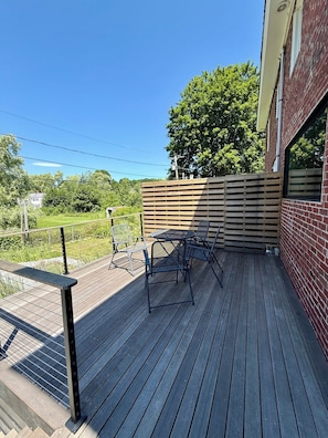 Eine Holzterrasse mit Tisch und Stühlen, einem Metallgeländer und einer Ziegelwand.