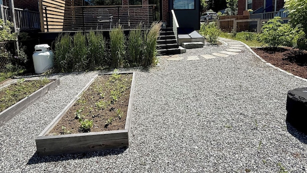 Un quartier résidentiel avec une allée en gravier, des jardinières surélevées en bois et une maison en briques au design moderne.