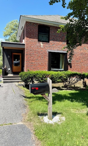 Ein zweistöckiges Ziegelhaus mit Haustür, Briefkasten und kleinem Vorgarten mit Hecke.