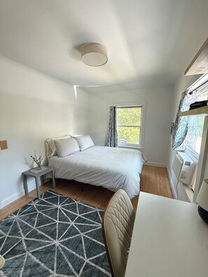 A bedroom with a bed, bedside table, and a window with curtains. - Sun-Filled Brick Townhouse Near Downtown Bath (Bath)