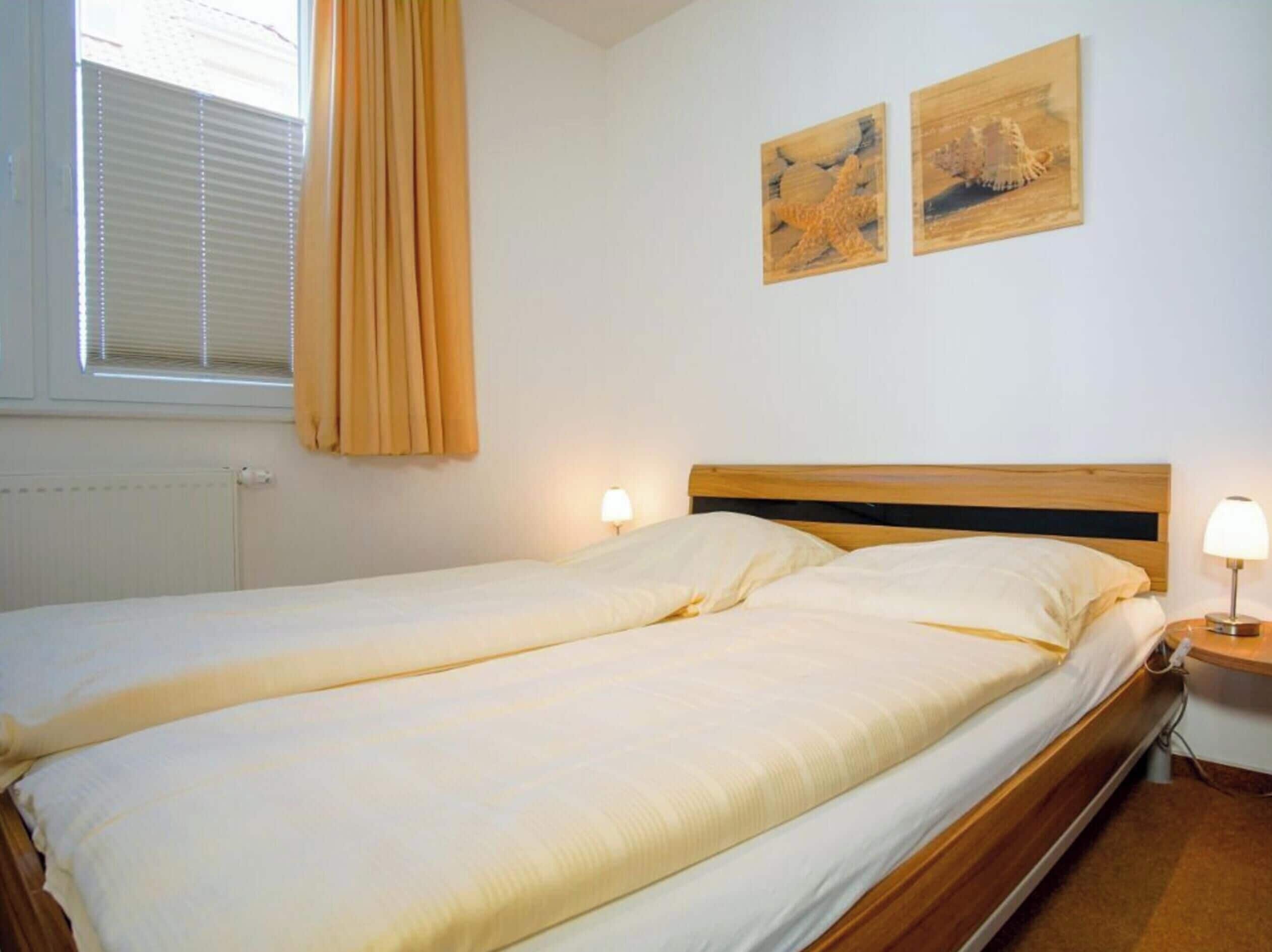 A single bed with a wooden headboard in a room with white walls. There are two wall-mounted lamps on either side of the bed.