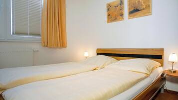 A single bed with a wooden headboard in a room with white walls. There are two wall-mounted lamps on either side of the bed.