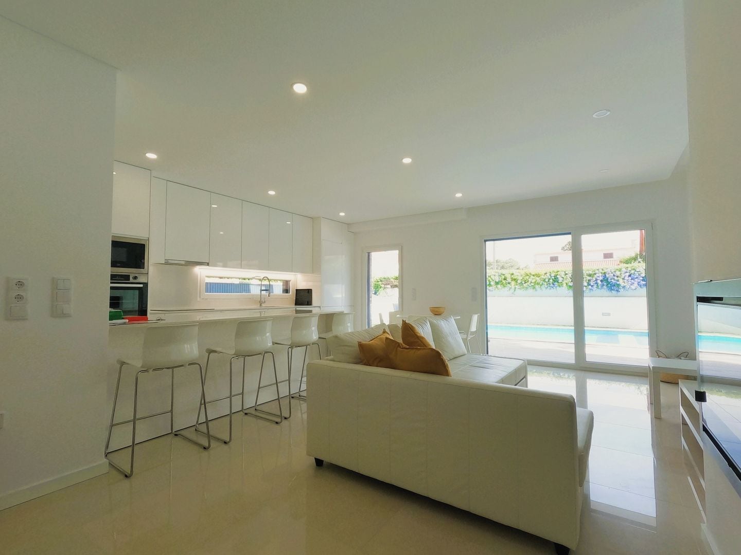 A modern kitchen with white cabinets, a bar area, and a large window overlooking a pool.