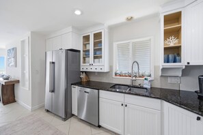 A modern kitchen with white cabinetry, stainless steel appliances, and a granite countertop. - 5BR Beachfront Escape | Private Beach Access (Cape Canaveral)