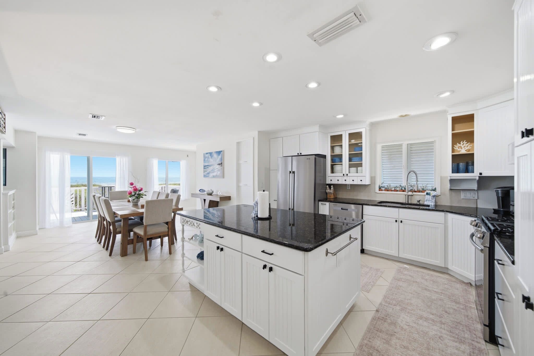 Una cocina moderna con armarios blancos, una isla central y un comedor con vistas.
