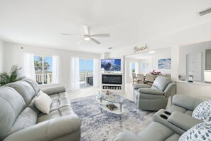Ein modernes Wohnzimmer mit einer Couch, einem Couchtisch und einem Fernseher. Es gibt einen Balkon mit Meerblick.