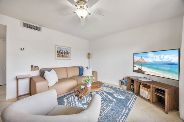 Un salon avec un canapé beige, une table basse, un téléviseur et une décoration murale sur le thème de la plage.