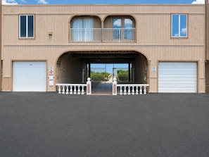 Un immeuble de deux étages avec un accès au garage, un balcon et une allée privée fermée par un portail.