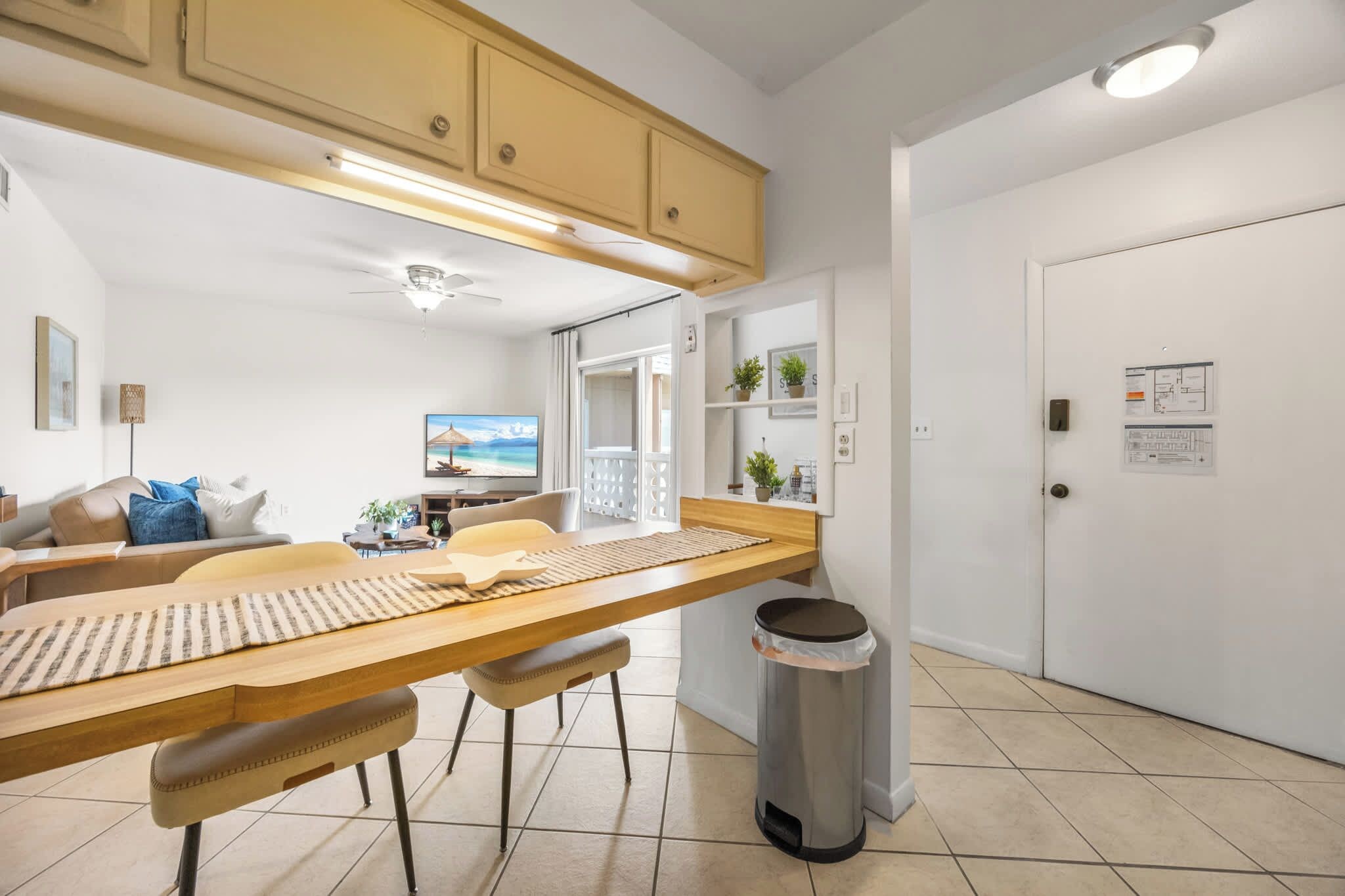 Une cuisine moderne avec une longue table en bois, des tabourets de bar et une poubelle.