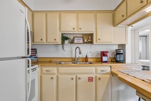 Une cuisine avec des meubles de couleur beige, un évier en acier inoxydable, une machine à café et un réfrigérateur.