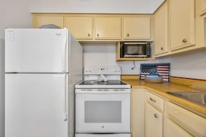 A compact kitchen with a white refrigerator, a microwave, and a stove. - The Diplomat 2BR with Pool and Beach Access (Cocoa Beach)