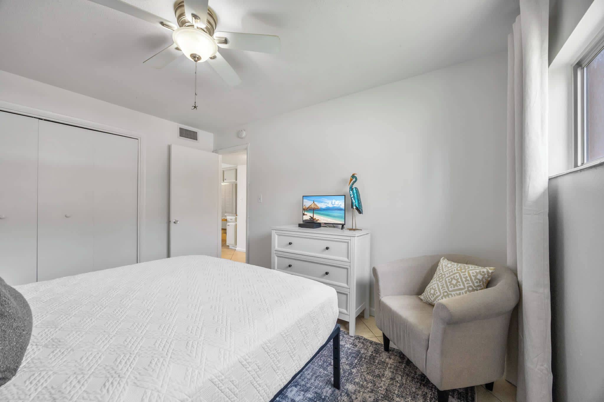 A bedroom with a bed, a dresser, a television, and a chair.