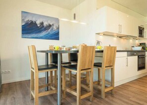A modern kitchen with a dining table and chairs, a painting on the wall, and a microwave.