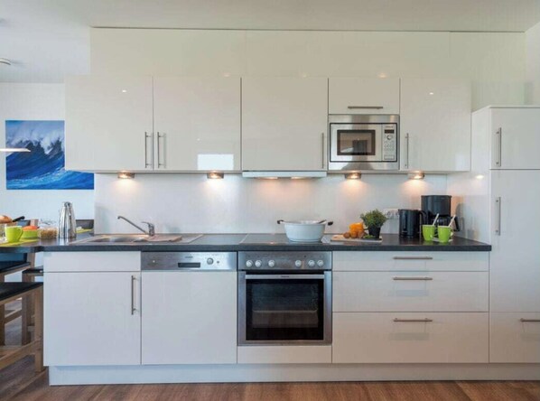 A modern kitchen with white cabinets, stainless steel appliances, and a central island with a sink and stove.