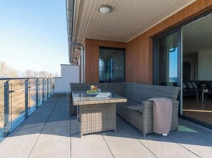 A balcony with a wicker sofa, a small table, and a bowl of fruit.