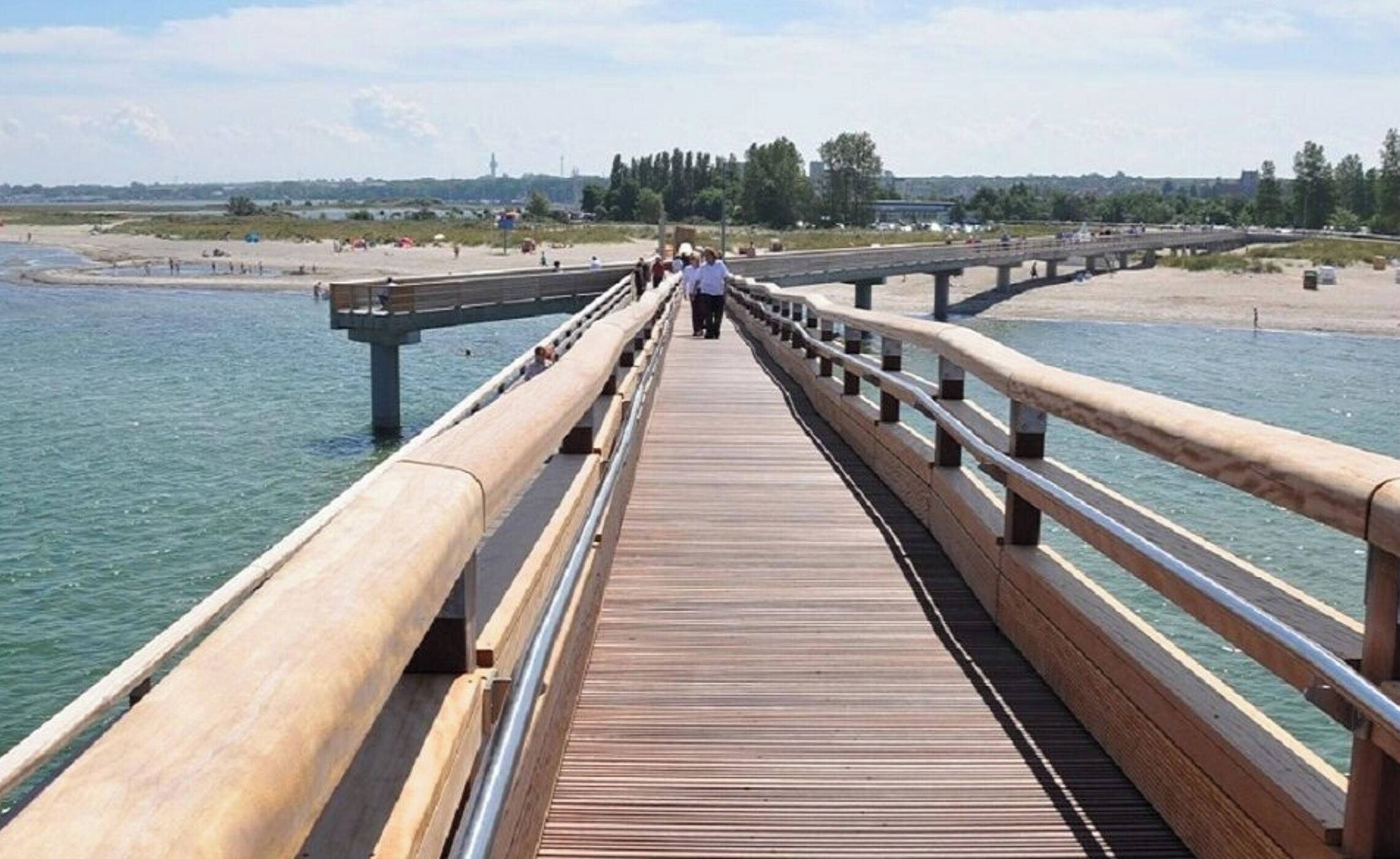 A wooden boardwalk leading to a beach with a clear view of the water and distant buildings.