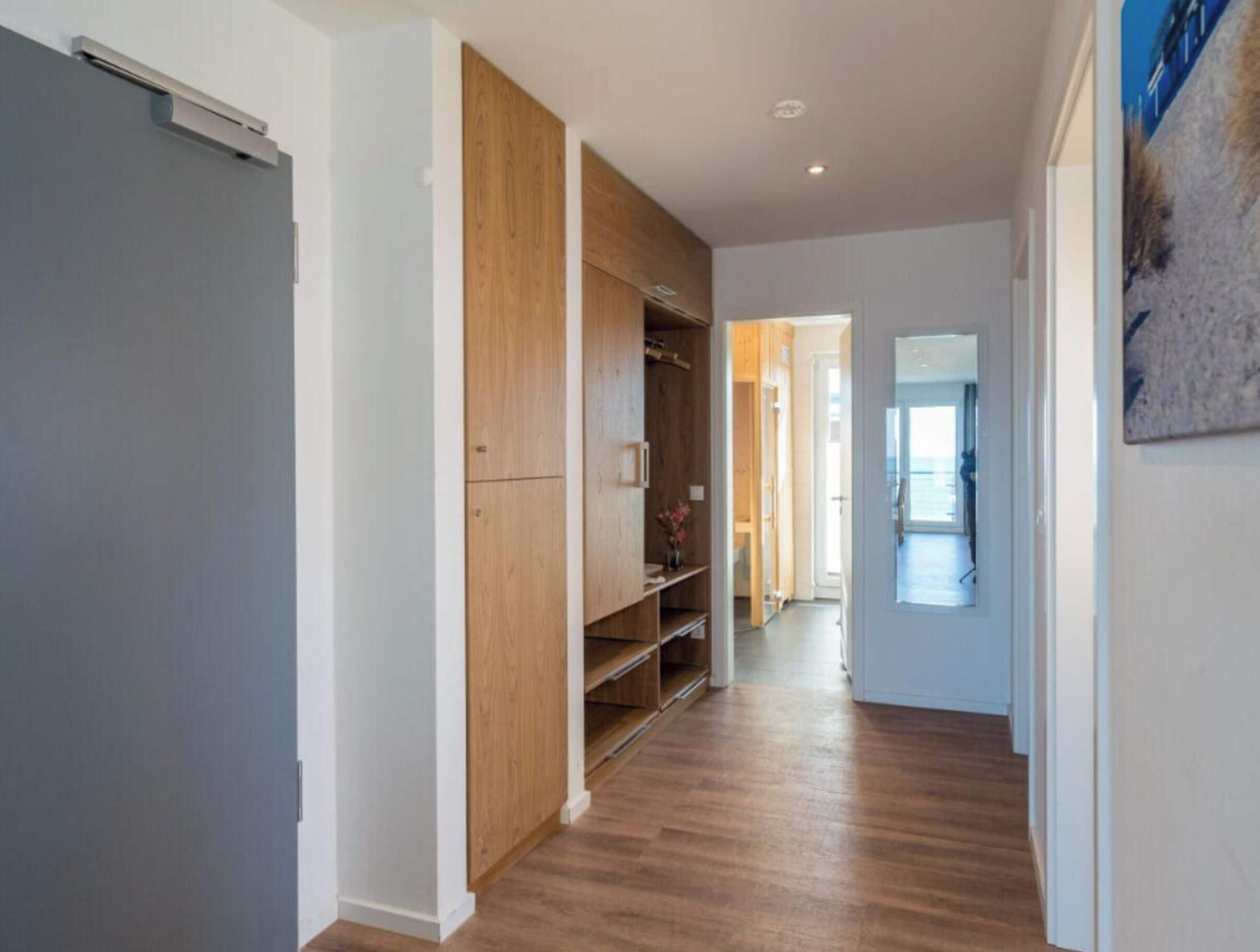 A hallway with wooden flooring, a built-in closet, and a door leading to another room.