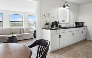 Een moderne keuken met witte kasten, een zwart aanrecht en uitzicht op het landschap door grote ramen.