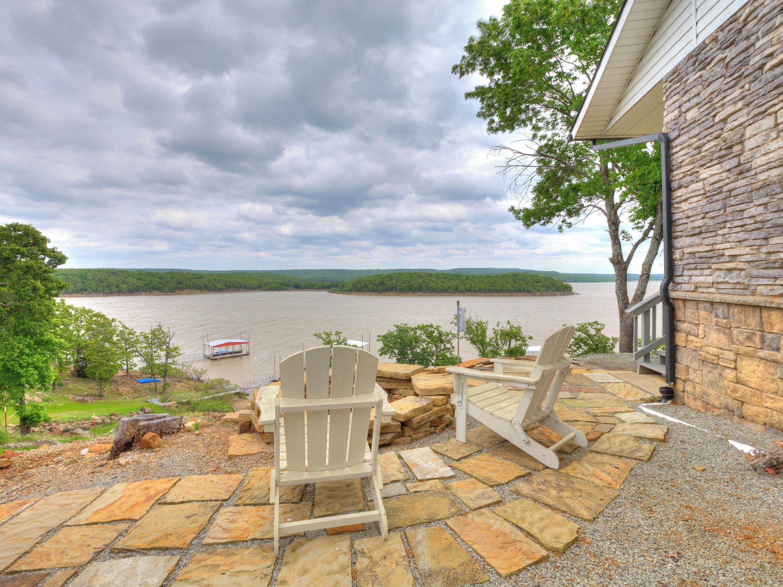 Une terrasse avec des fauteuils Adirondack donnant sur une rivière, un mur de pierres et un quai pour bateaux.