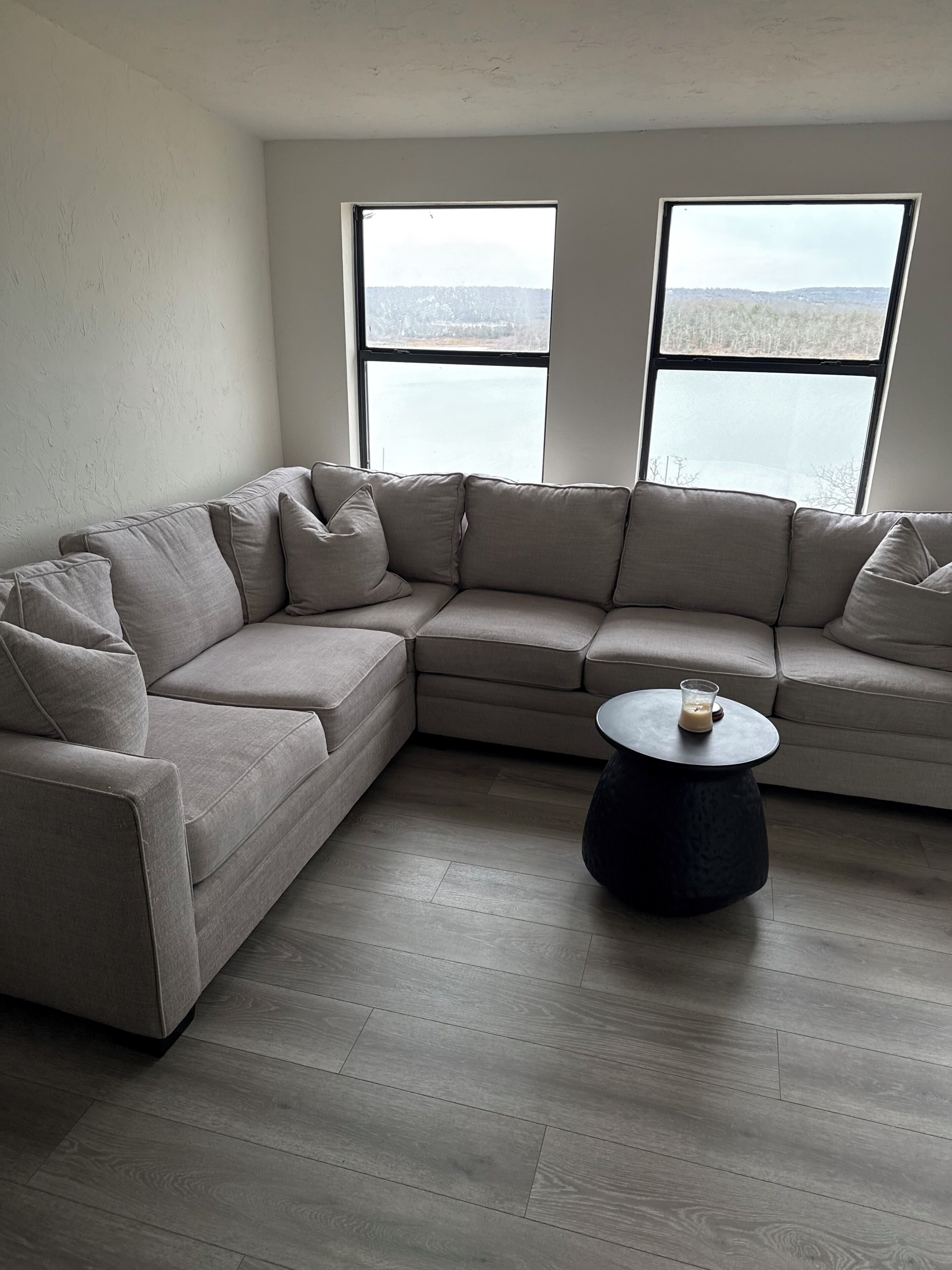 Una sala moderna con un sofá seccional, una mesa redonda y amplias ventanas que ofrecen vista a un paisaje nevado.