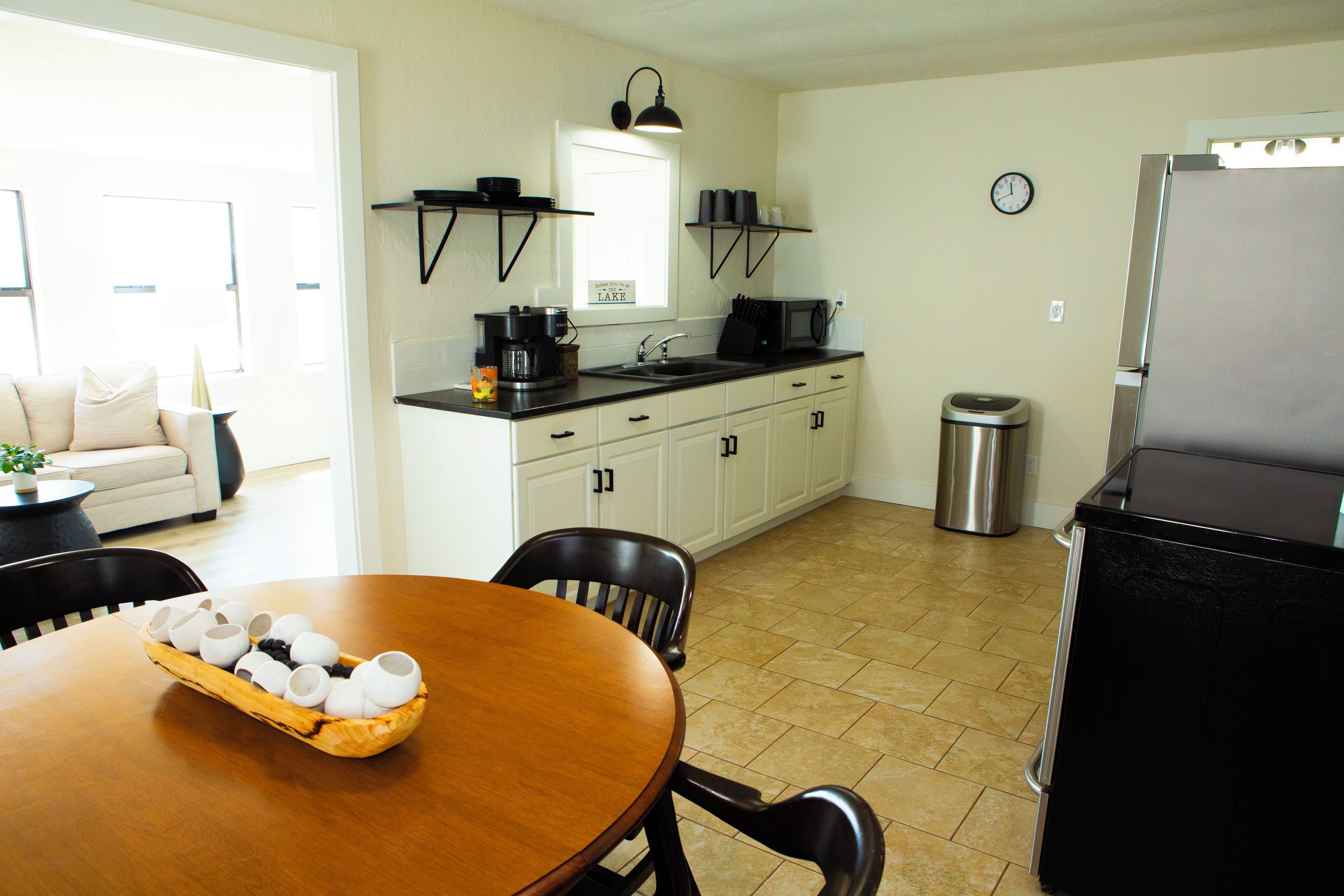 A kitchen with a dining table, chairs, a coffee maker, a microwave, and a trash can.
