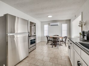 A modern kitchen with stainless steel appliances, a dining area with a table and chairs, and a window with blinds. - Charming lake front 2-bedroom cottage with AC on peaceful Lake Eufaula, OK. (Canadian)