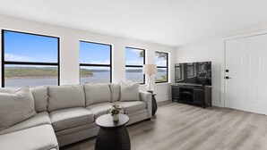 Ein modernes Wohnzimmer mit einer Couch, einem Couchtisch, einem Fernseher und großen Fenstern mit Seeblick.