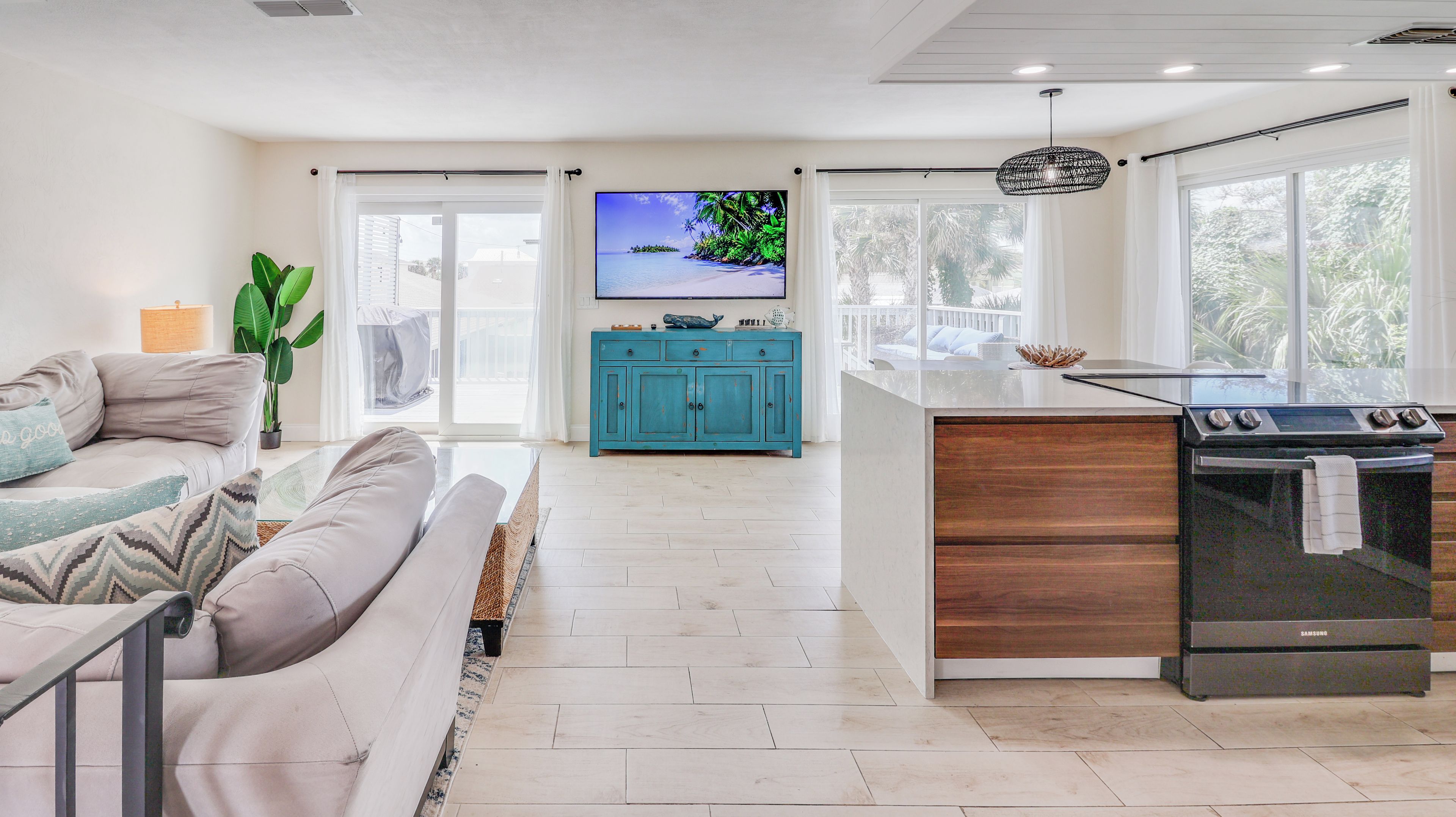 A modern kitchen with a built-in oven, a dining area with a sofa, and a TV displaying a tropical scene.