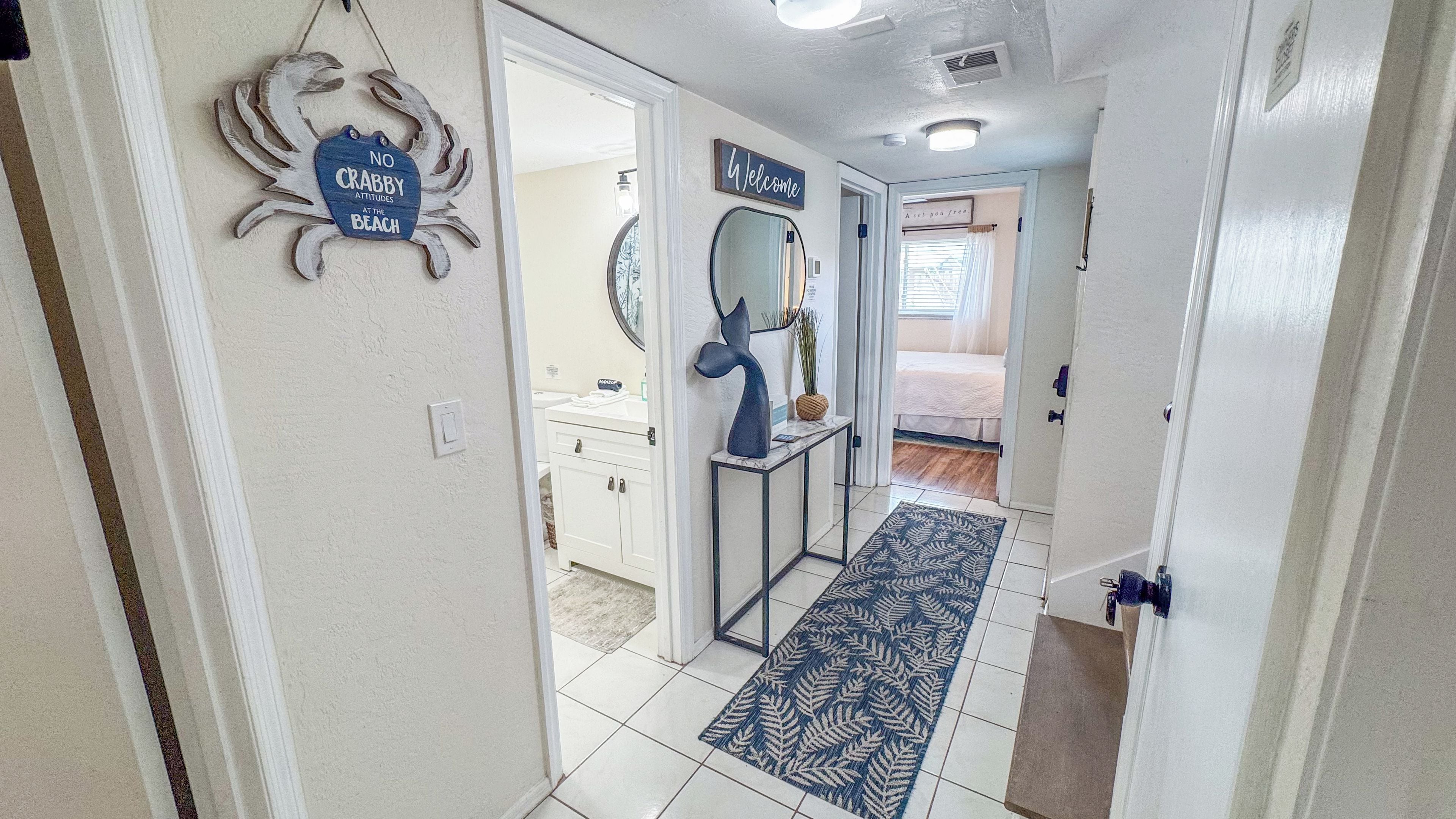A hallway with a welcome sign, a mirror, a console table, and a patterned rug.