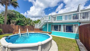 A backyard with a swimming pool, a wooden deck, and a house with a balcony. - A-Wave From It All #1 - Pet-Friendly Pool Home (New Smyrna Beach)
