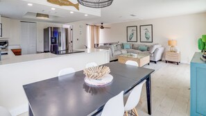 A modern kitchen with a refrigerator, a dining table with chairs, a sofa, and a coffee table. - A-Wave From It All #1 - Pet-Friendly Pool Home (New Smyrna Beach)