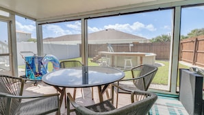 Une terrasse couverte avec une table ronde et des chaises en osier, donnant sur un jardin avec un espace barbecue.